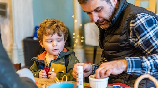 Young boy and father sat together at table doing Christmas craft activities.